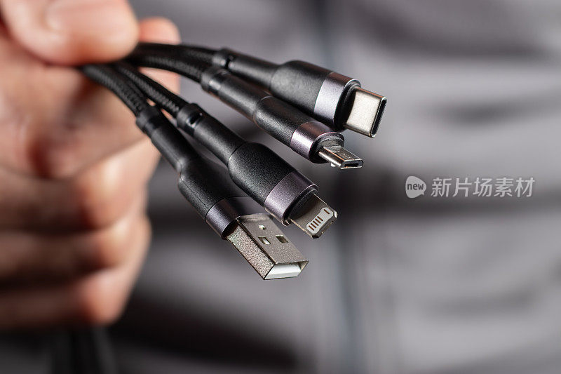 这只手握着一根通用USB电缆。USB Type C, Micro USB, USB lightning